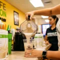 Herbalife Nutrition Club staff preparing a Formula 1 protein shake in a modern wellness cafe.